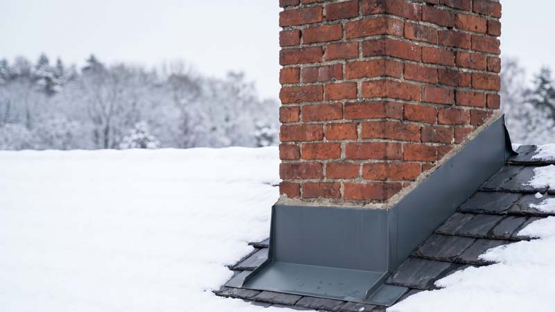 Классическая кирпичная дымовая труба с защитным металлическим примыканием на зимней крыше