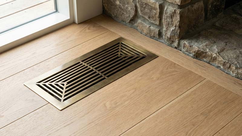 латунная вентиляционная решетка в деревянном полу рядом с каменным основанием камина для подачи воздуха